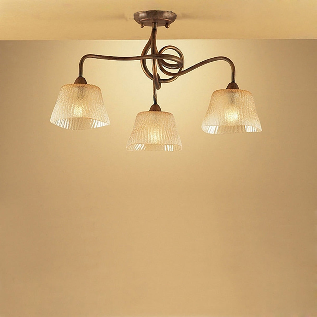 Mantra Tentacle 3 light semi-flush ceiling light with rustic gold intertwined metal arms and frosted amber glass shades, mounted to a warm-toned ceiling.