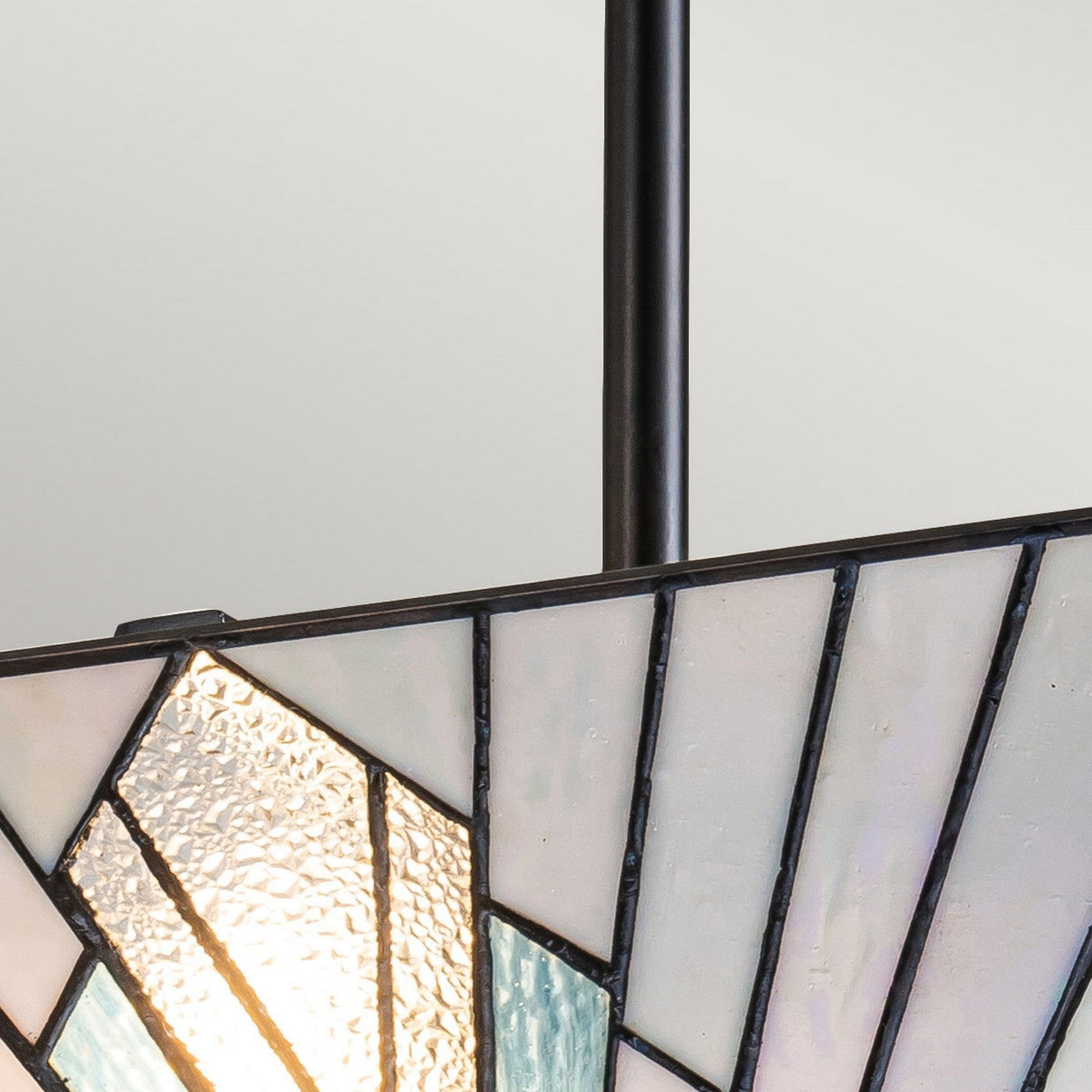 Close-up of the Alderley 2 Light Trio Mount Tiffany Pendant in Vintage Bronze, showcasing its geometric pattern. The design includes sections of white, textured clear, and light blue glass. A light bulb inside subtly highlights the varied glass textures, while a black metal rod extends from the top to add a touch of vintage bronze charm.