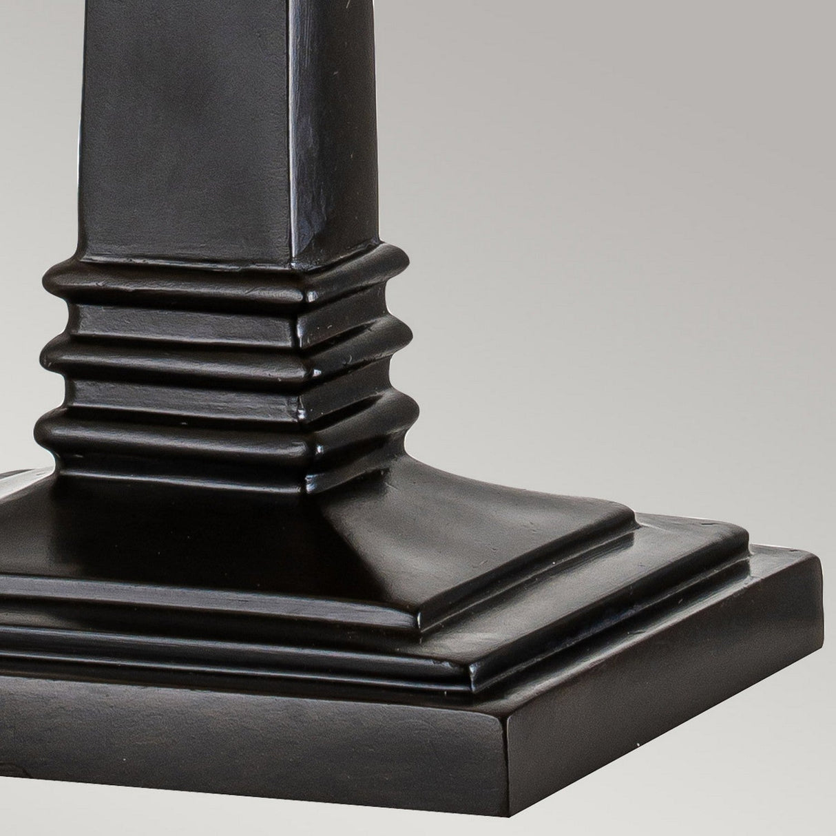 Close-up of the Alderley 1 Light Large Table Lamp in Vintage Bronze, featuring a black, square ornamental base with an Art Deco-inspired stepped design and a vertical column rising from it. The surface is smooth and polished, lending a modern, minimalist aesthetic against a plain light gray background.