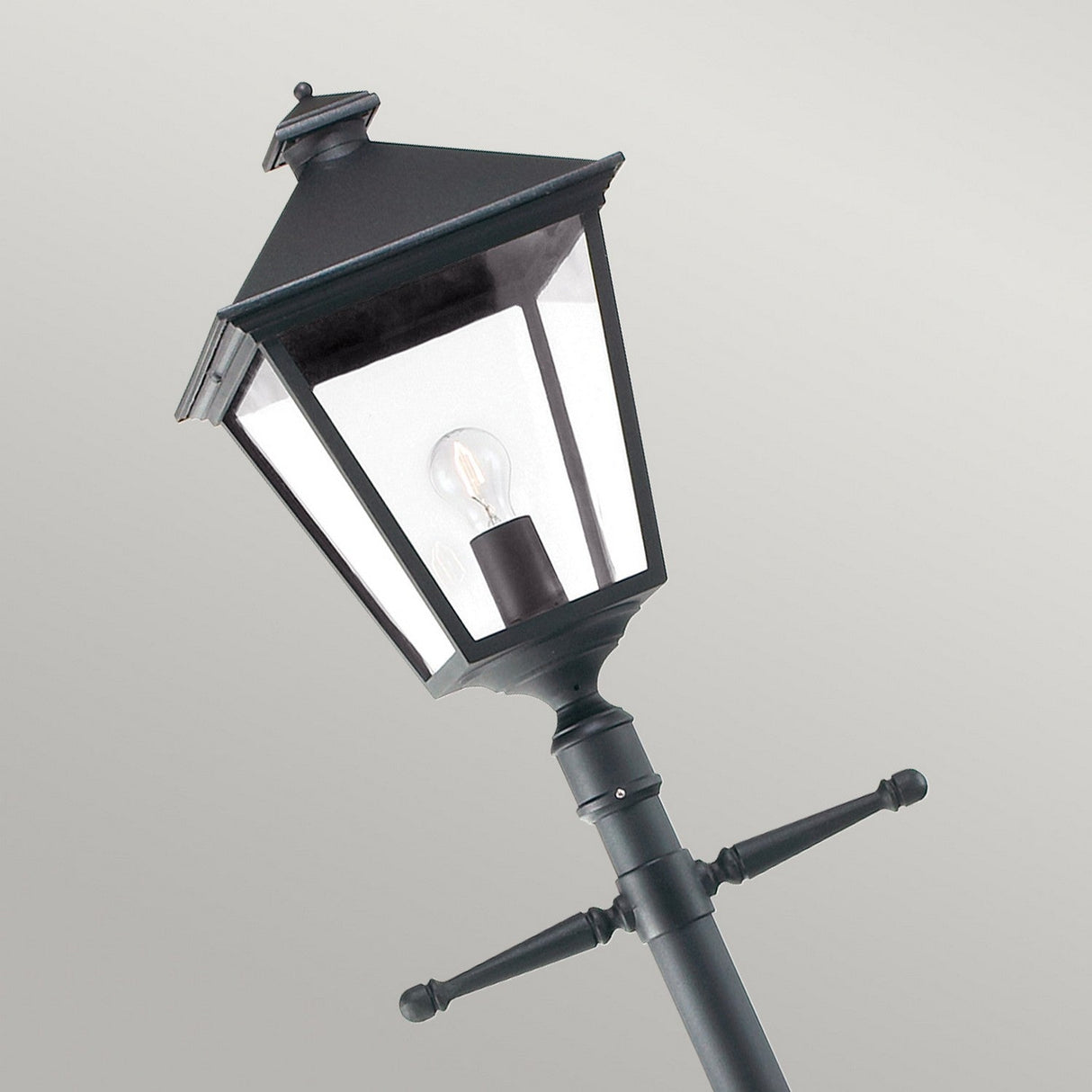The Turin Large 1 Light Single Post in black is a vintage-style street lamp made from die-cast aluminum, showcasing a lantern design that features a visible light bulb inside. Set against a gray background, this outdoor lighting fixture has an IP54 rating and two horizontal bars that enhance its elegance.