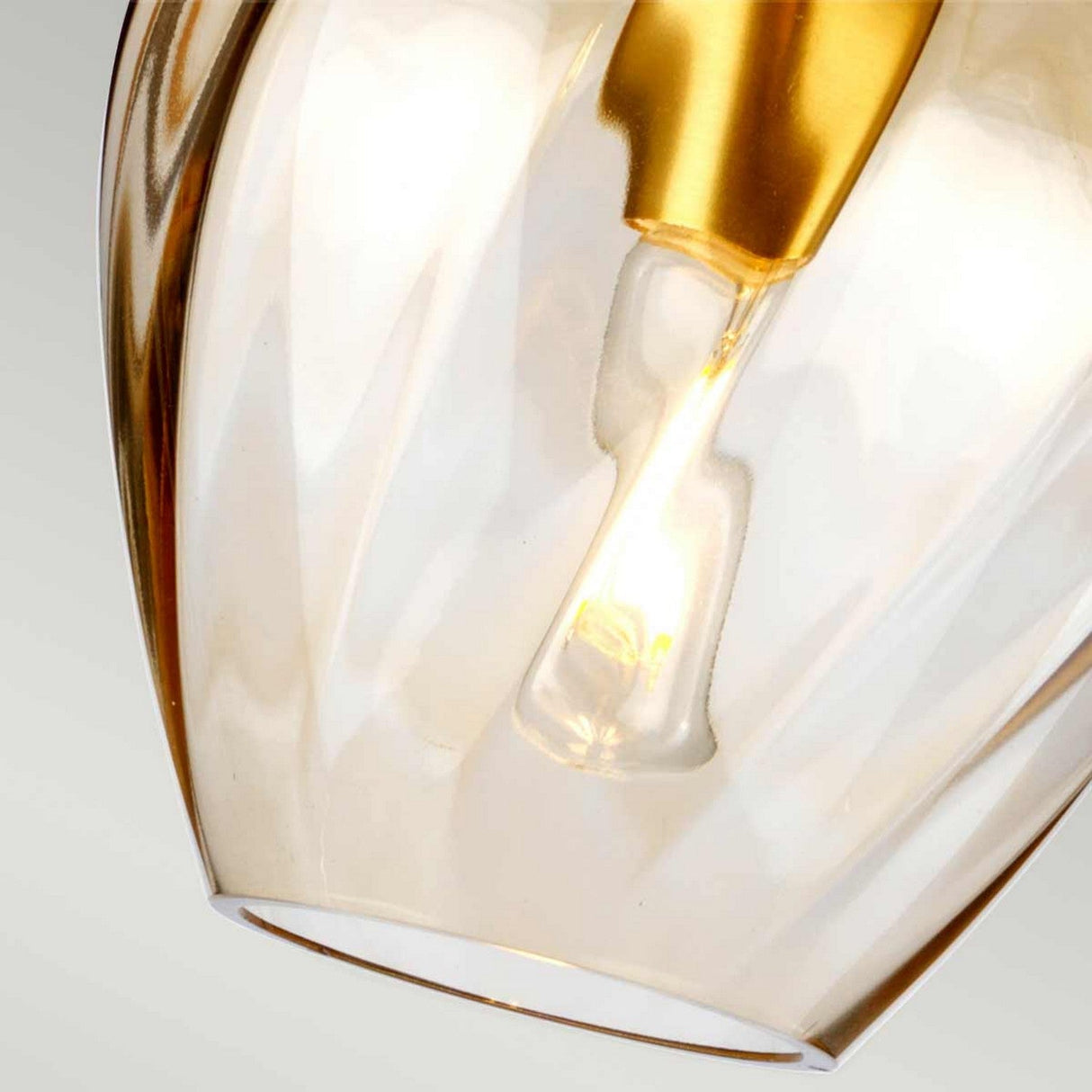 Close-up of the Tiber 1 Light Pendant in Brushed Brass and Amber Glass, showcasing its glowing design. The smooth amber glass surface beautifully reflects the soft light, while the background remains softly blurred.