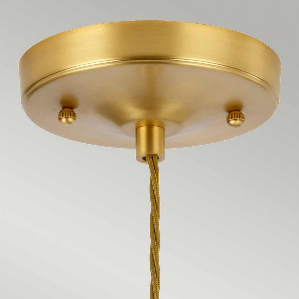 A close-up of the Tiber 1 Light Pendant in Brushed Brass/Amber Glass showcases a polished surface with a round canopy and twisted cord. The fixture is adorned with two small decorative knobs on the side and accented by elegant brushed brass details.