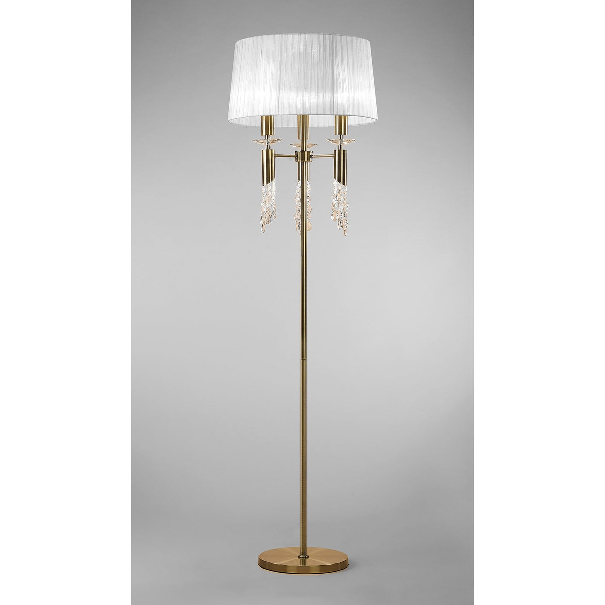 The Tiffany 6 Light Crystal Floor Lamp features a tall brass base, a round stand, white pleated shade, and sparkling crystal pendants below the shade, set against a plain gray background.