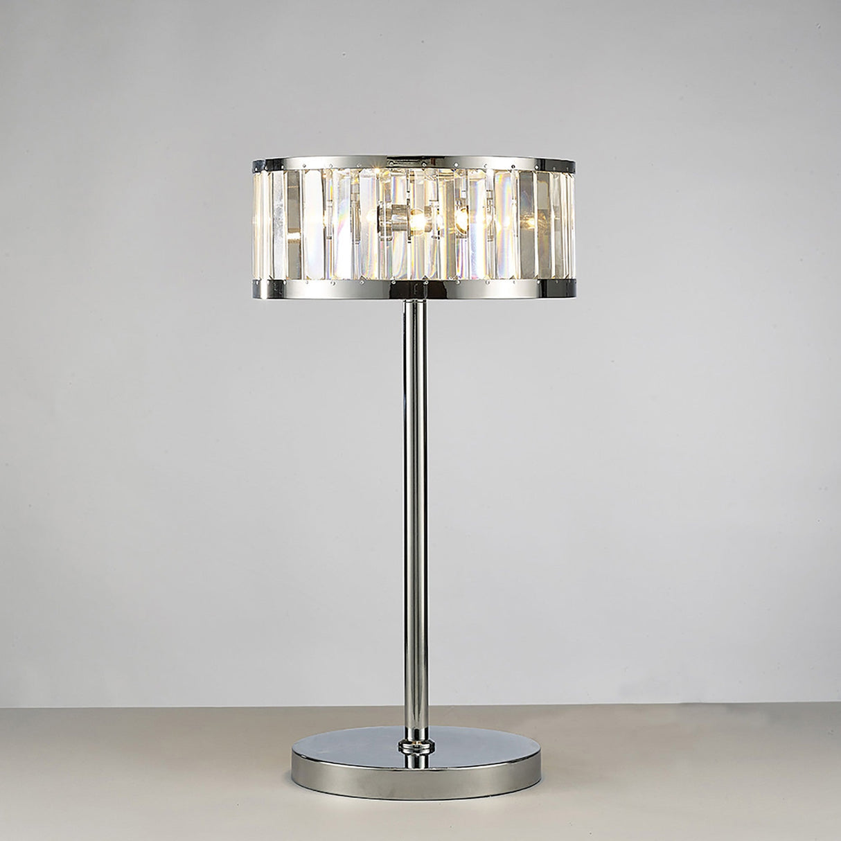 The Torre 3 Light Crystal Table Lamp features a polished chrome base and vertical clear glass panels, emitting a soft, warm glow against a light gray background.