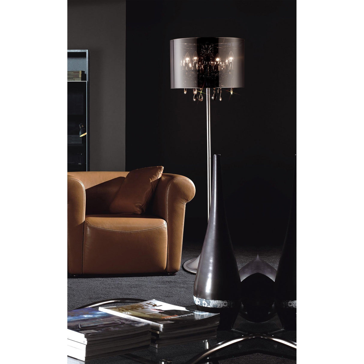 A modern living room with a brown leather armchair, the Trace 4 Light Crystal Floor Lamp – Chrome with Chrome Shade, a glass coffee table stacked with magazines, and black decorative vases set against dark walls.