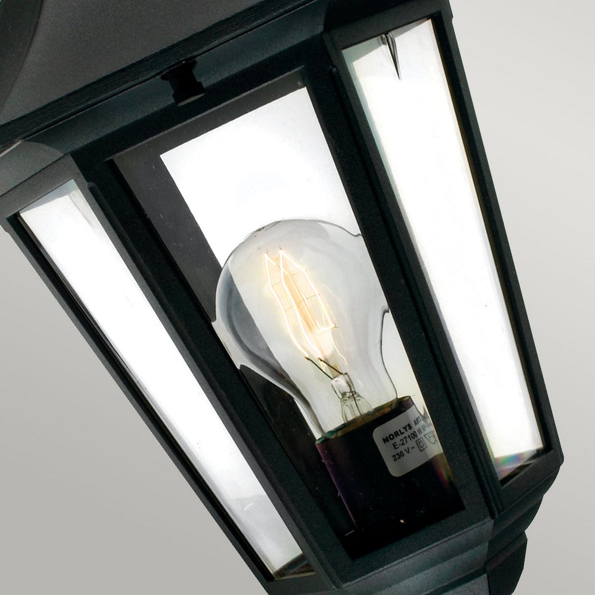 A close-up view of the Valencia Outdoor 1 Light Up Lantern in black, crafted from die-cast aluminium with a clear glass panel, showcasing a light bulb inside. The lit bulb illuminates the interior against a neutral background, highlighting the lantern's weather-resistant finish.