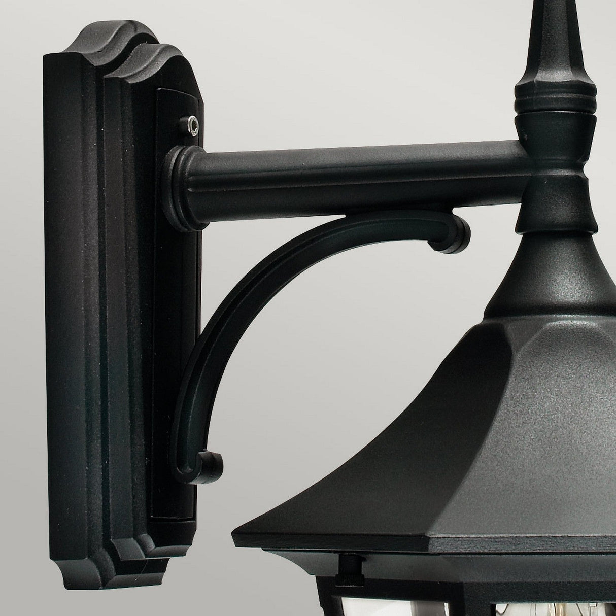Close-up of the Valencia Outdoor 1 Light Down Lantern in black, crafted from die-cast aluminium and showcasing a classic design. This fixture features a decorative curved arm, rectangular backplate, and a sloped roof detail. The weather-resistant lantern is displayed against a plain, light gray background.