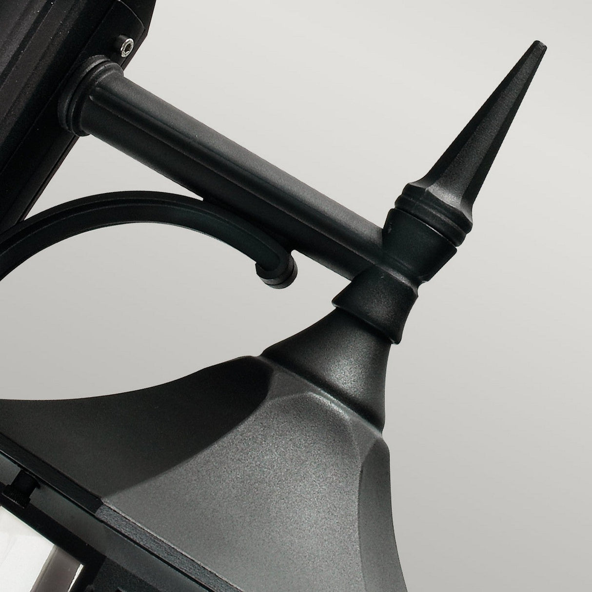 A close-up of the Valencia Outdoor 1 Light Down Lantern in black, crafted from die-cast aluminum with a pointed top and mounted on a wall. This sleek, weather-resistant design showcases a curved arm and detailed craftsmanship against a plain background.
