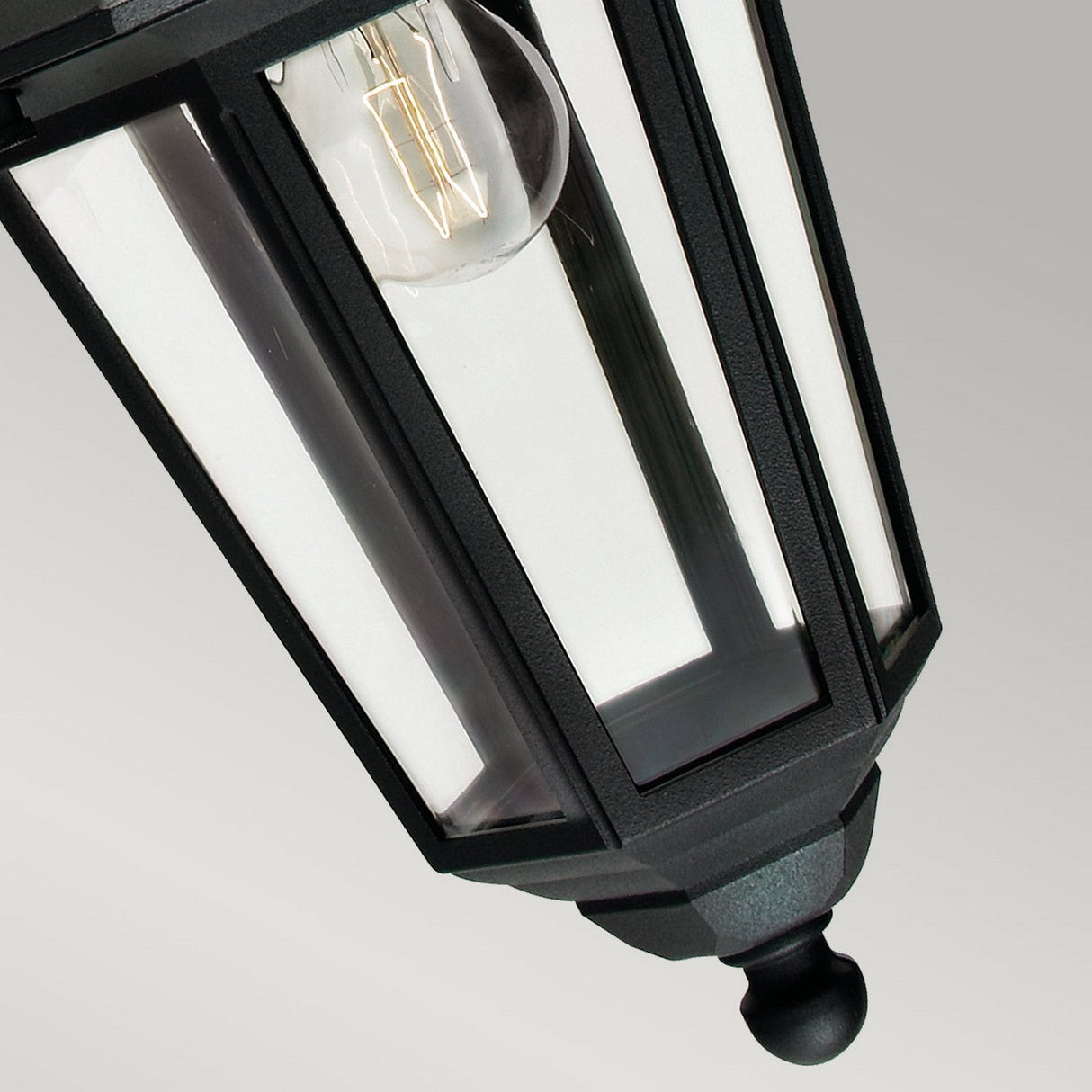 Close-up of the Valencia Outdoor 1 Light Down Lantern in black, made from weather-resistant die-cast aluminium. Featuring clear glass panels and a visible light bulb inside, it is set against a neutral background to highlight its modern geometric design.