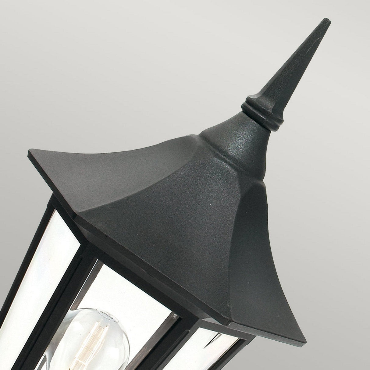A close-up of the Valencia 1 Light Pedestal in black, crafted from durable die-cast aluminum with clear glass panels. This elegant outdoor lighting piece stands against a light gray background, highlighting its classic design.