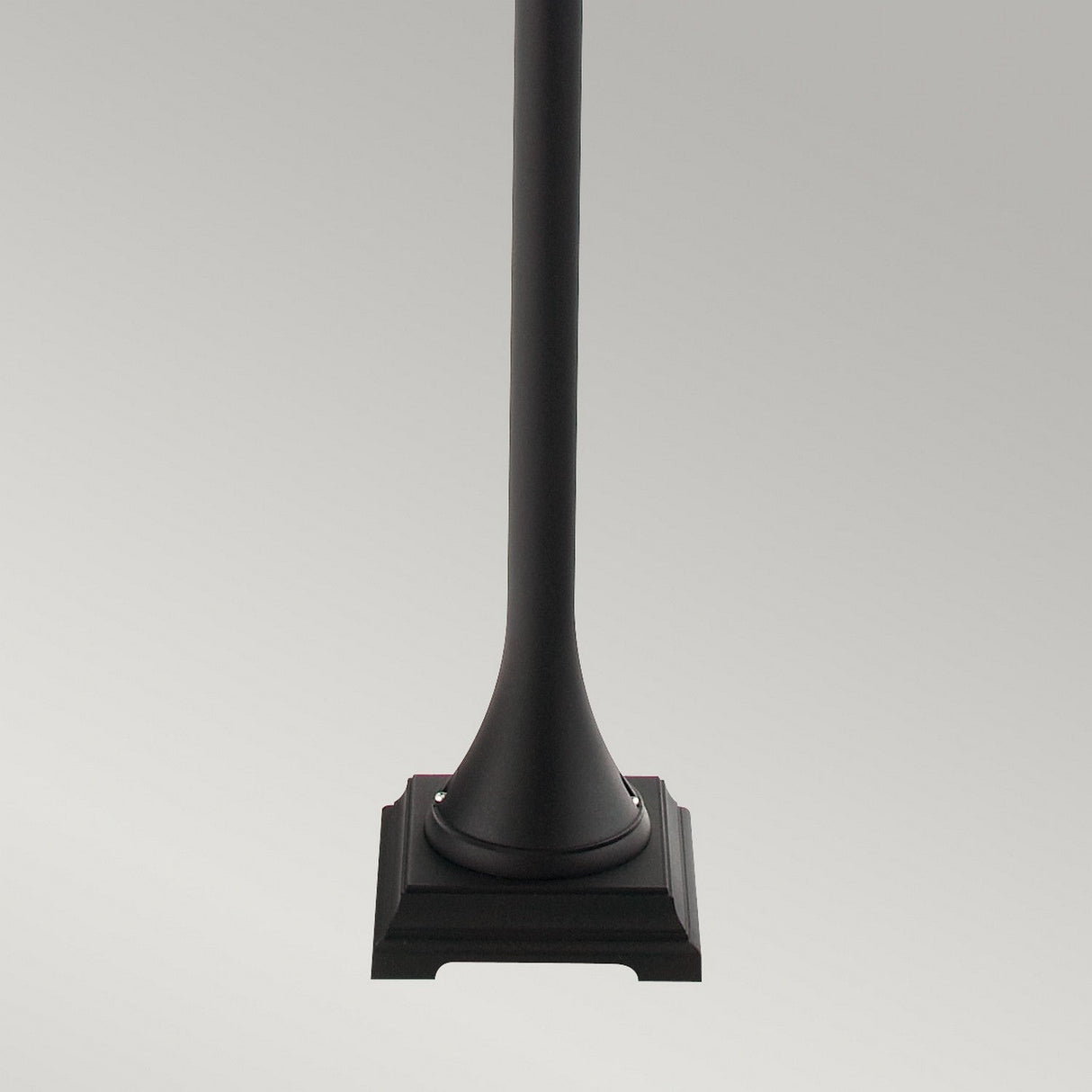 The image highlights the base of a black metal pole, resembling the sophisticated Valencia 1 Light Pillar - Black, complete with a square pedestal. Perfect for illuminating garden pathways, it stands out against a smooth, light gray gradient backdrop.