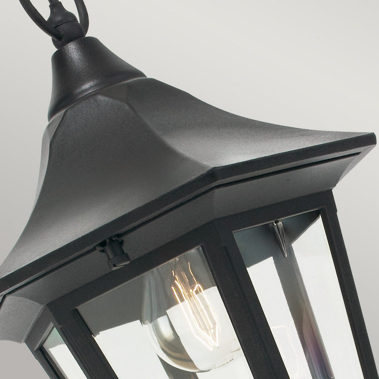 An up-close view of the Valencia Outdoor 1 Light Chain Pendant - Black, showcasing its black die-cast aluminium frame and clear glass panels. The fixture elegantly displays a single light bulb inside and hangs gracefully from a black chain against a simple gray backdrop.