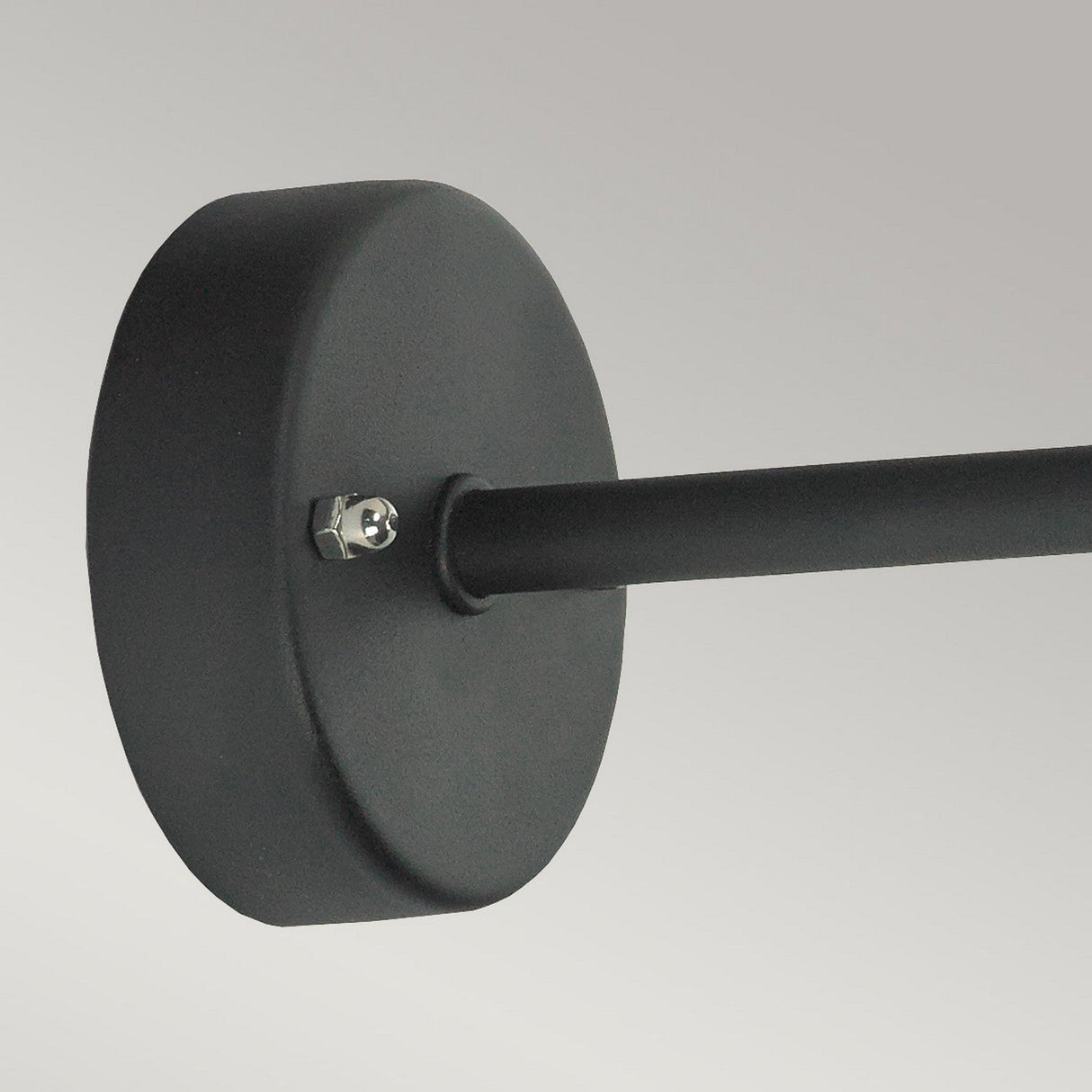 A close-up of the Vansbro Outdoor 1 Light Wall Lantern - Black, crafted from galvanized steel with a cylindrical rod extending from it, secured by a visible bolt. The piece boasts an IP55 rating for durability. The background is a plain gray color.