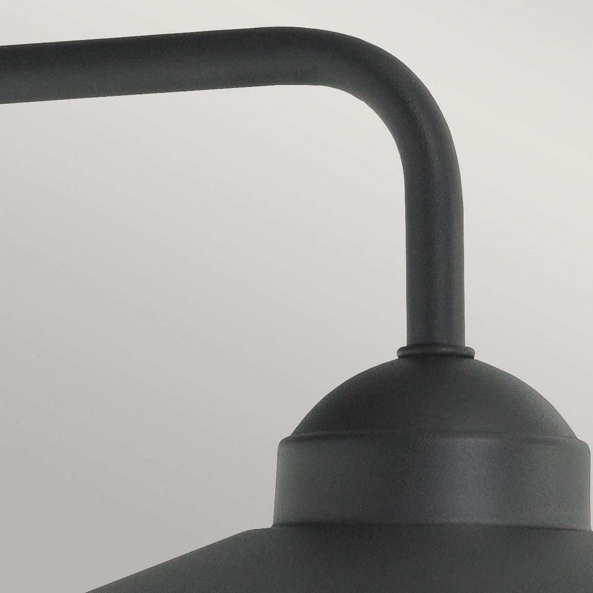 A close-up of the Vansbro Outdoor 1 Light Wall Lantern in matte black metal showcases its curved arm and dome-shaped top against a light gray background. This minimalist, modern design features sleek lines and a smooth finish, reminiscent of an outdoor wall lantern crafted from galvanized steel.