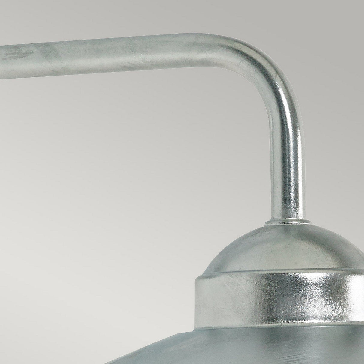 Close-up of the Vansbro Outdoor 1 Light Wall Lantern in silver, featuring a curved arm and dome-shaped shade in an industrial metallic style. Its brushed finish resembles galvanized steel, set against a simple light gray backdrop.