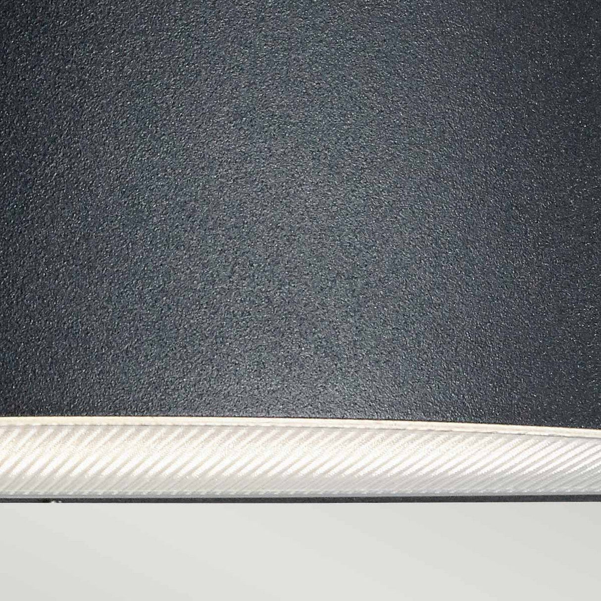 Close-up of the Vasa Outdoor 1 Light Wall Light in Graphite, featuring a textured black finish with a white interior edge, crafted from die-cast aluminum, set against a light gray background.