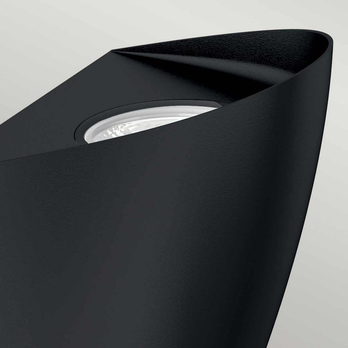 Close-up of the Vendela Outdoor LED Wall Light in black, showcasing its minimalist design and energy-efficient lighting. The light is slightly tilted, highlighting its sleek curves and textured surface. With an IP65 rating, the bulb can be seen within the fixture's protective casing.