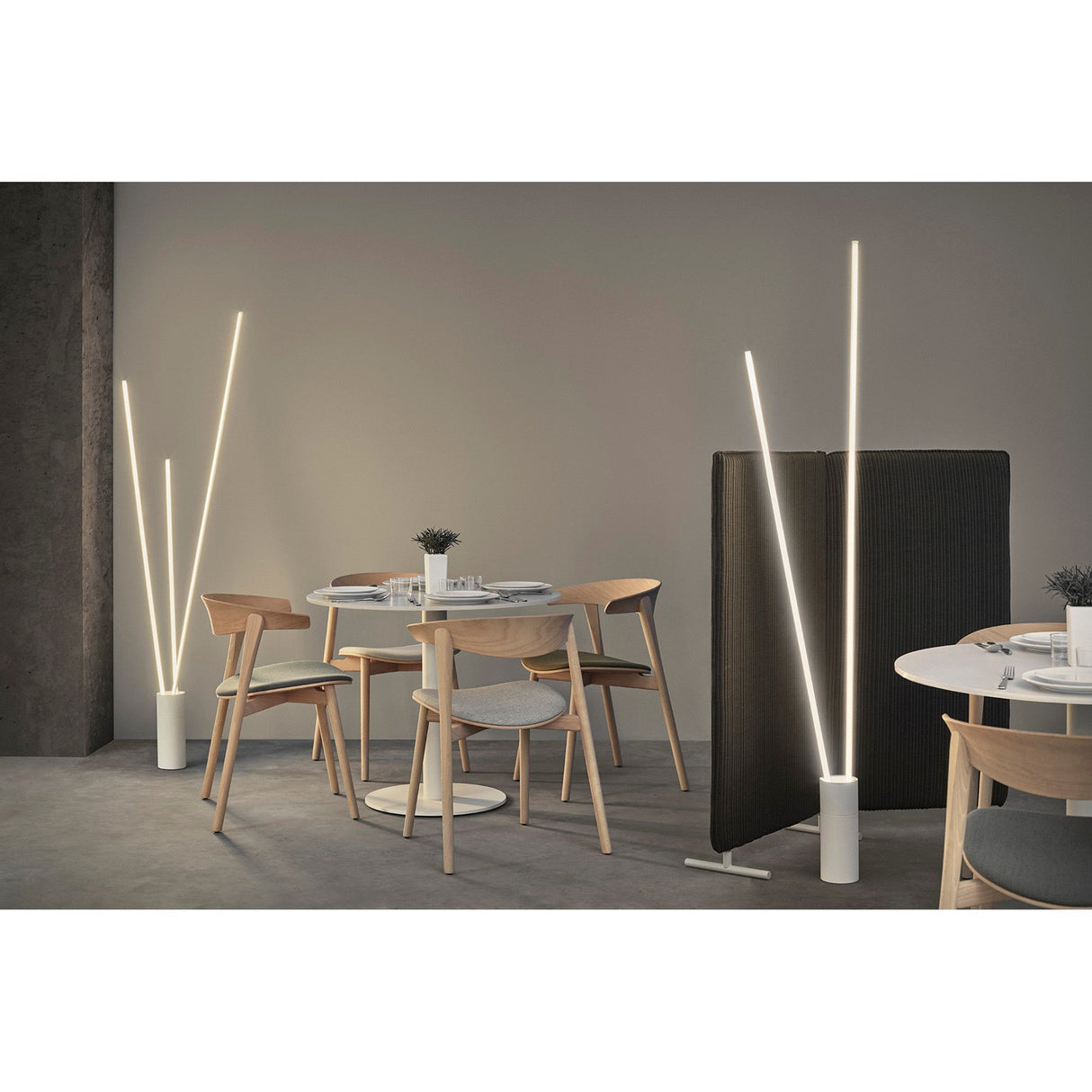 Modern minimalist dining area with round tables, wooden chairs, and Vertical Dimmable LED Floor Lamp 44W 3000K - White providing soft light. A small partition divides the space; each table features a small plant centerpiece.
