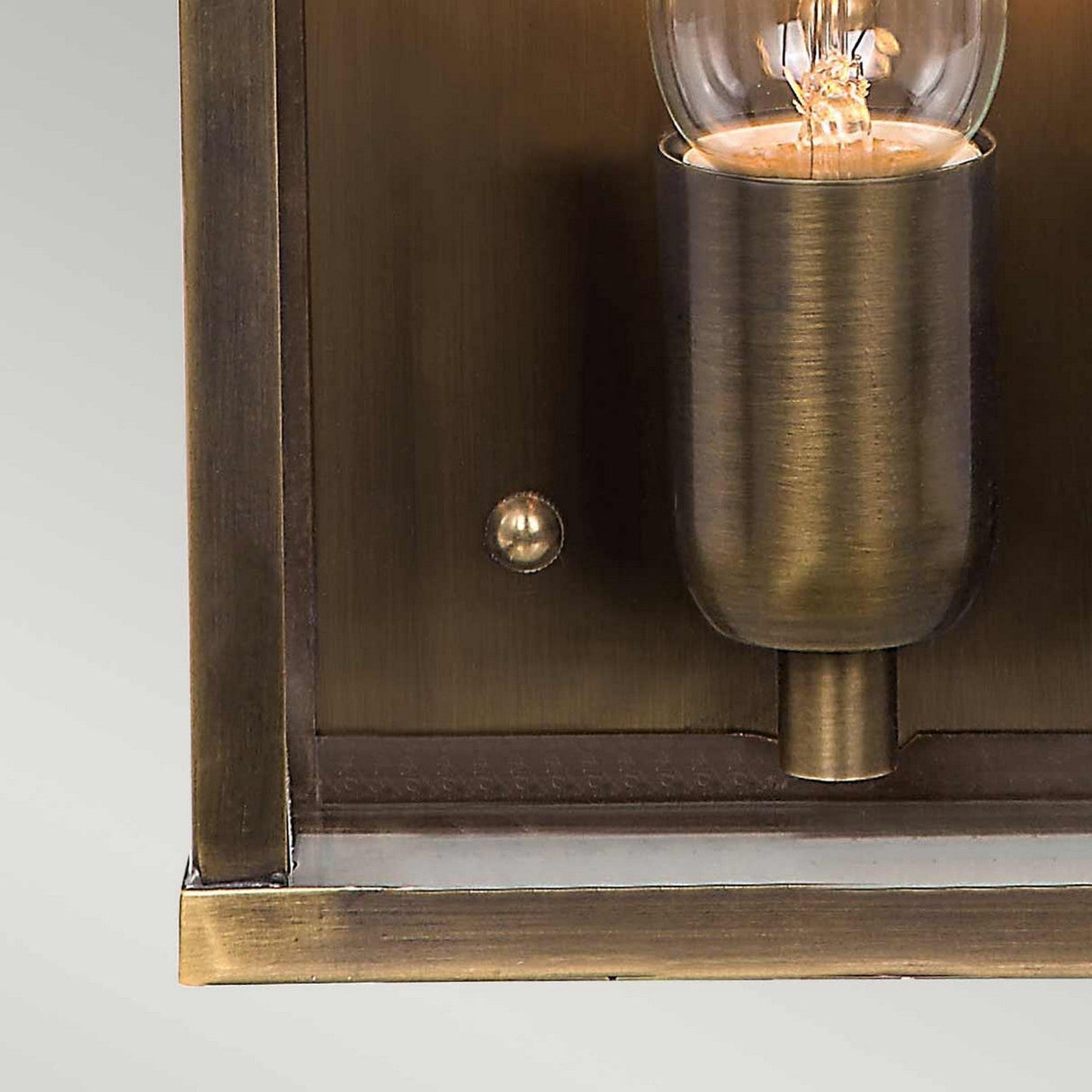 Close-up of the Victoria 1 Light Outdoor Wall Light - Aged Brass, a vintage-style wall sconce showcasing a clear, exposed bulb with visible filaments. Featuring an aged brass finish and a rectangular bronze backplate, this IP44 rated fixture offers a warm, industrial aesthetic.
