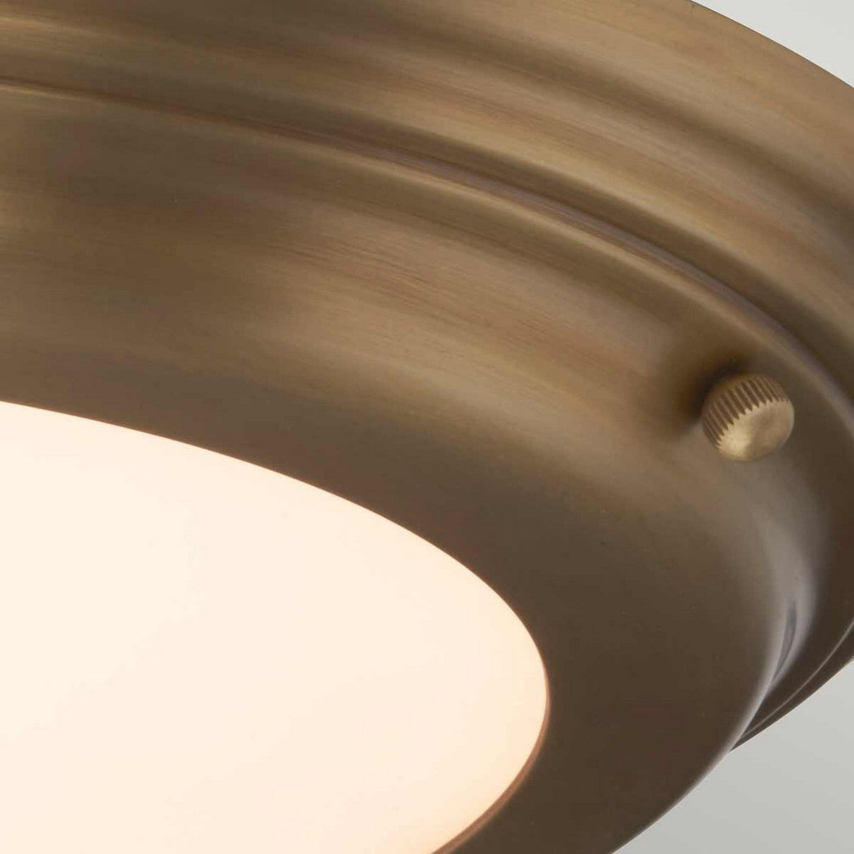 Close-up of the Welland LED Light Flush in aged brass, featuring a circular design. The elegant knob on its edge enhances its sophistication, and the IP54 rating guarantees durability. Its softly illuminated light creates a warm ambiance.