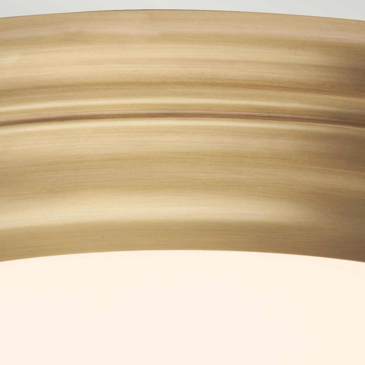 A close-up of the Welland LED Light Flush in aged brass showcases a smooth, curved beige surface with subtle horizontal light and dark bands, offering a soft and warm visual effect.