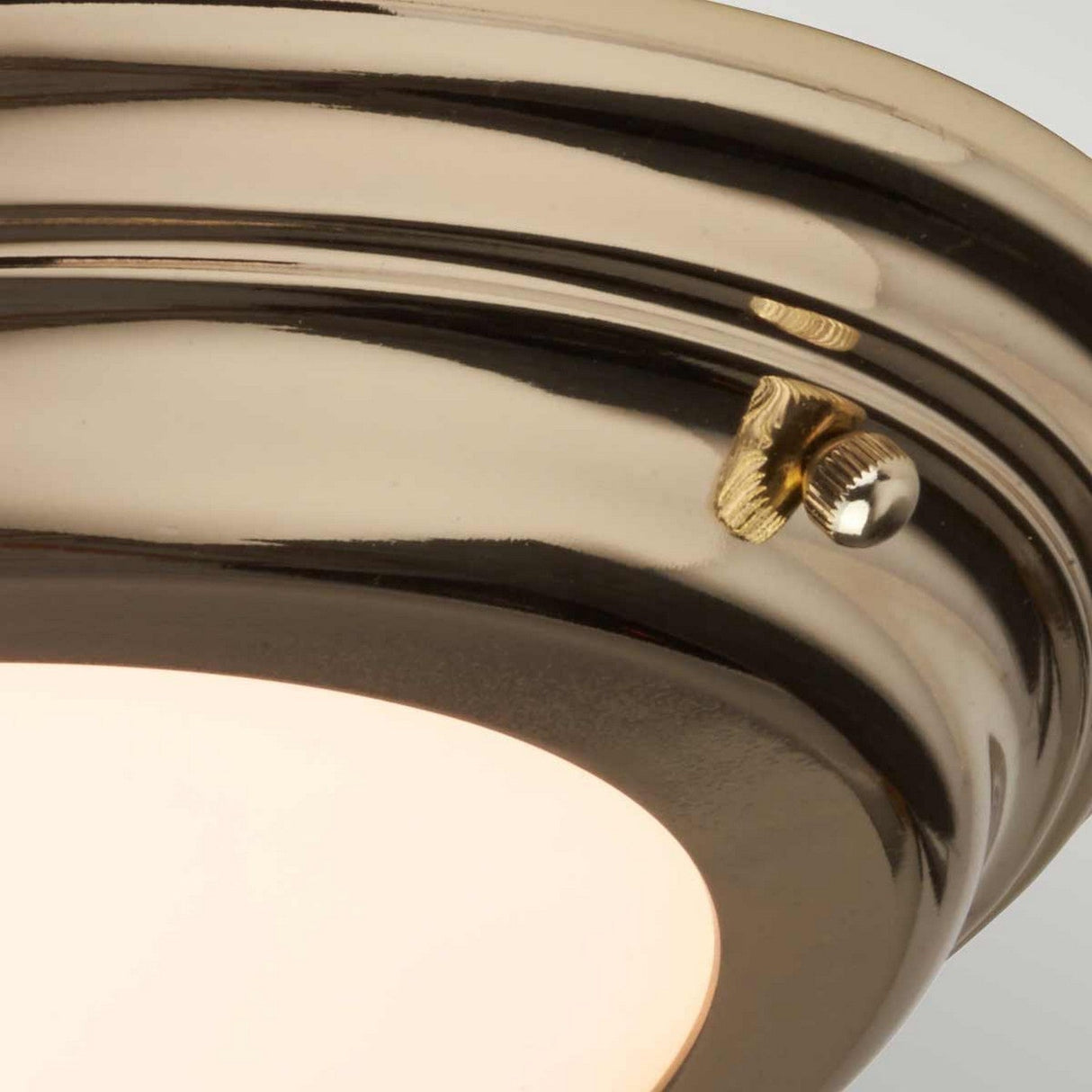 Close-up of the Welland LED Light Flush in a polished brass finish, featuring a round ceiling light fixture with a frosted glass diffuser. The design includes a small decorative screw on its side and boasts an IP54 rating for added durability.
