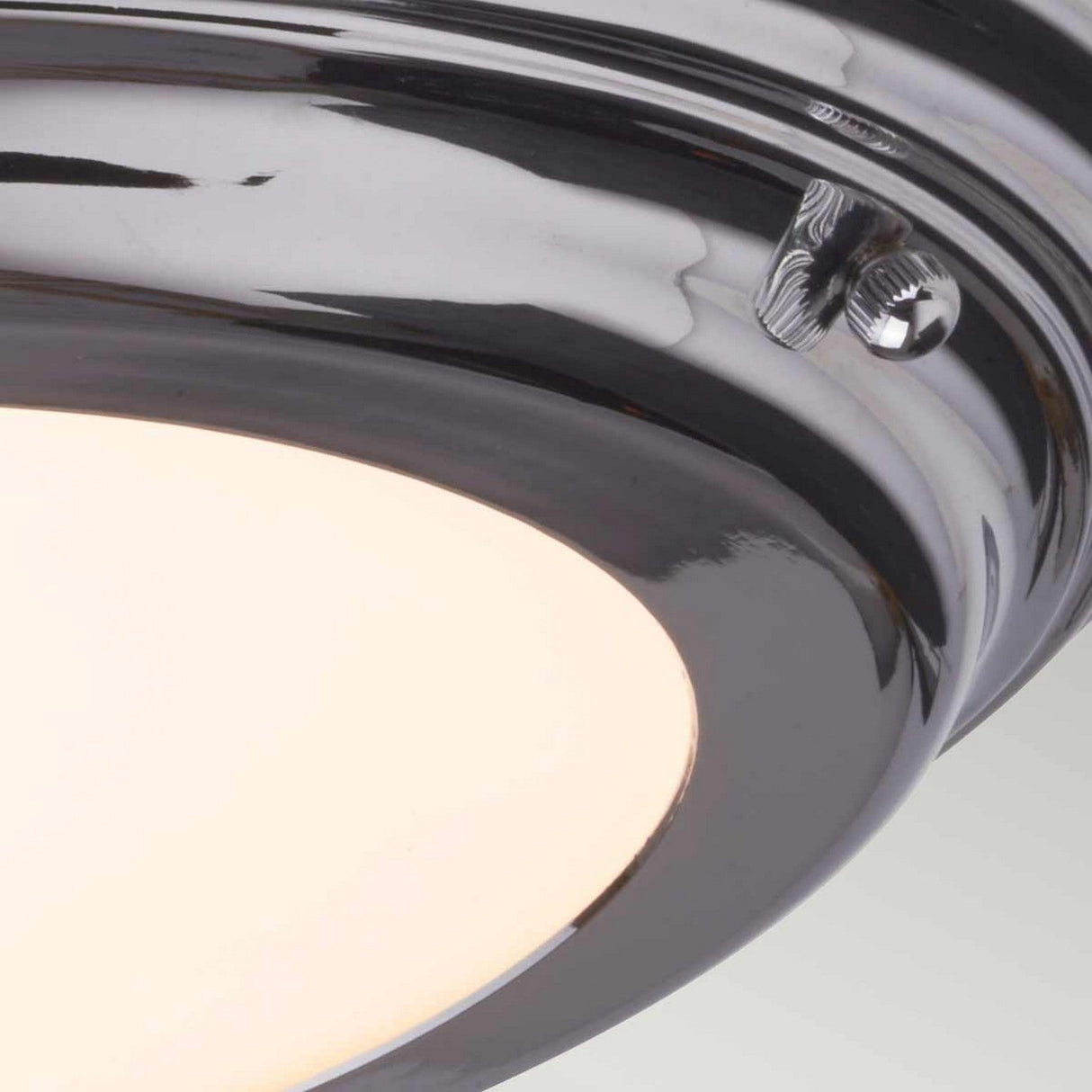 Close-up of the Welland LED Light Flush in polished chrome, rated IP54, with a frosted glass cover and mounted on a ceiling. The fixture showcases a shiny metallic rim and includes a small screw to secure the cover. When illuminated, it emits a soft, diffused glow.