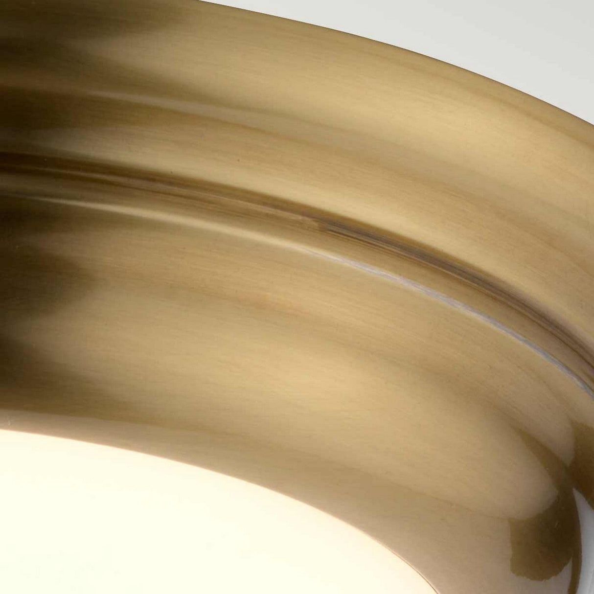 Close-up of the Welland LED Light Mini Flush in aged brass, showcasing its metallic and glossy curved surface with soft reflections and shadows accentuating its smooth texture.