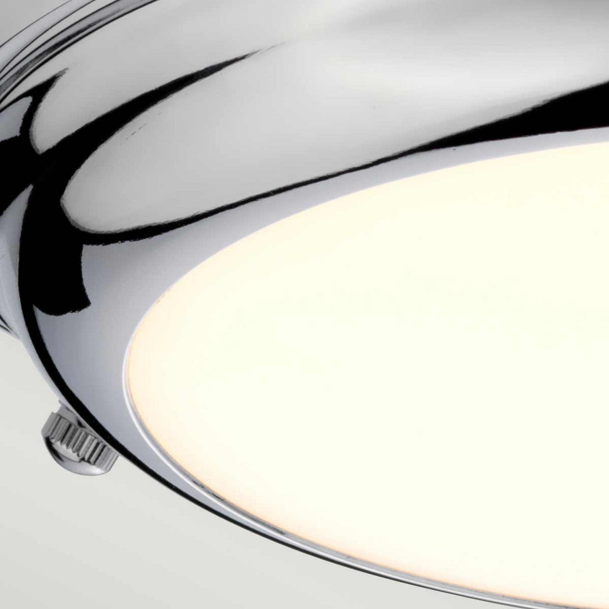 Close-up of the Welland LED Light Mini Flush, featuring a polished chrome frame and a smooth, frosted glass cover. The LED light is turned on, casting a soft, warm glow against a plain, neutral background.