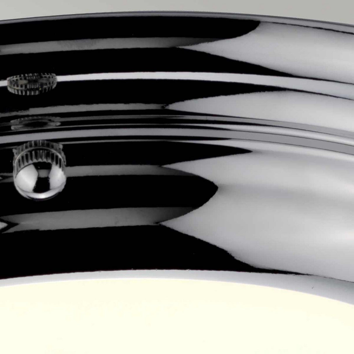 A close-up of the Welland LED Light Mini Flush in polished chrome showcases its curved design as it beautifully reflects its surroundings. The LED light from below emits a soft glow, accentuating its sleek elegance against a gently blurred background.