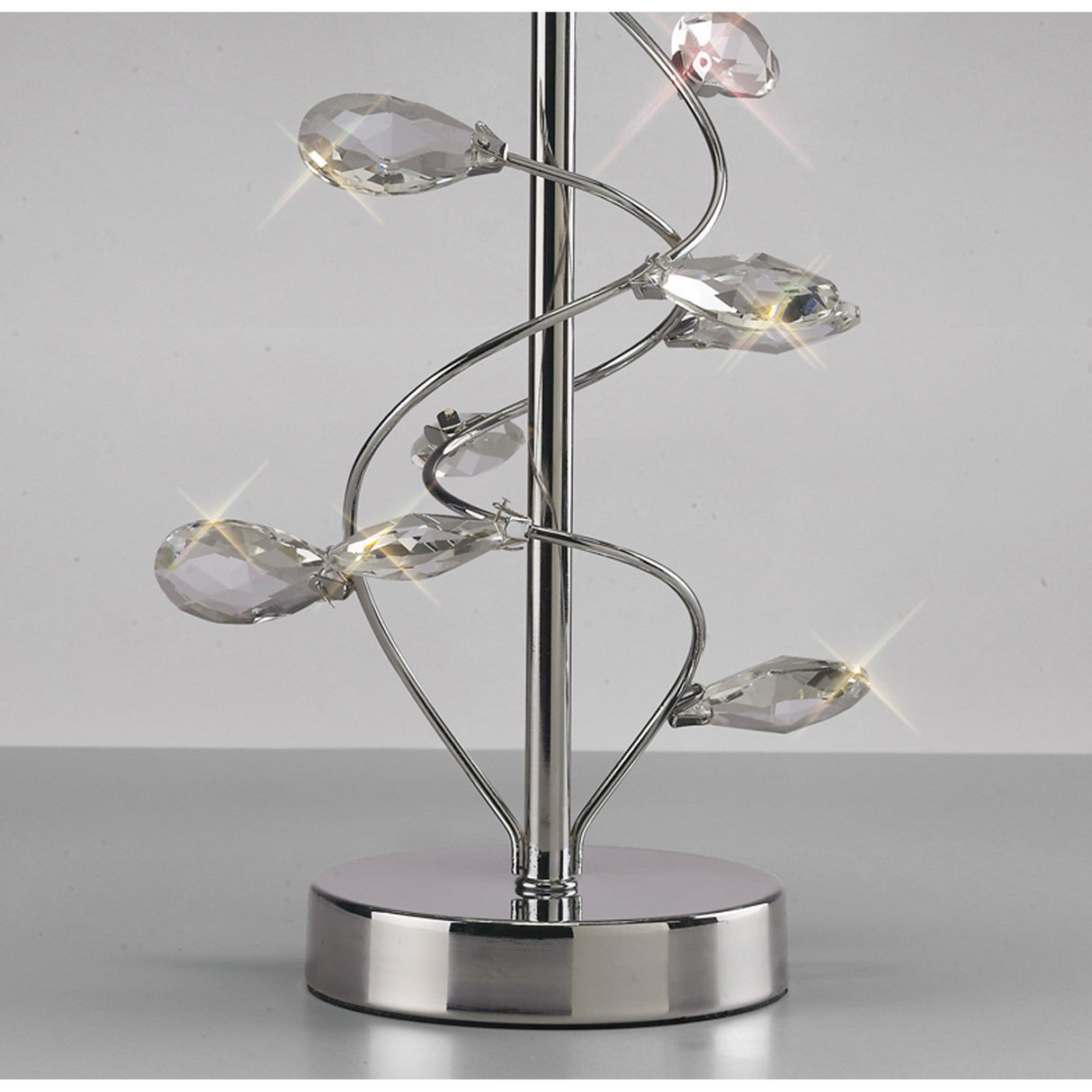 The Willow 1 Light Crystal Table Lamp features a shiny chrome base and stem with clear crystal leaves spiraling around, reflecting light for small sparkling effects. It comes with a cream shade for a contemporary touch.