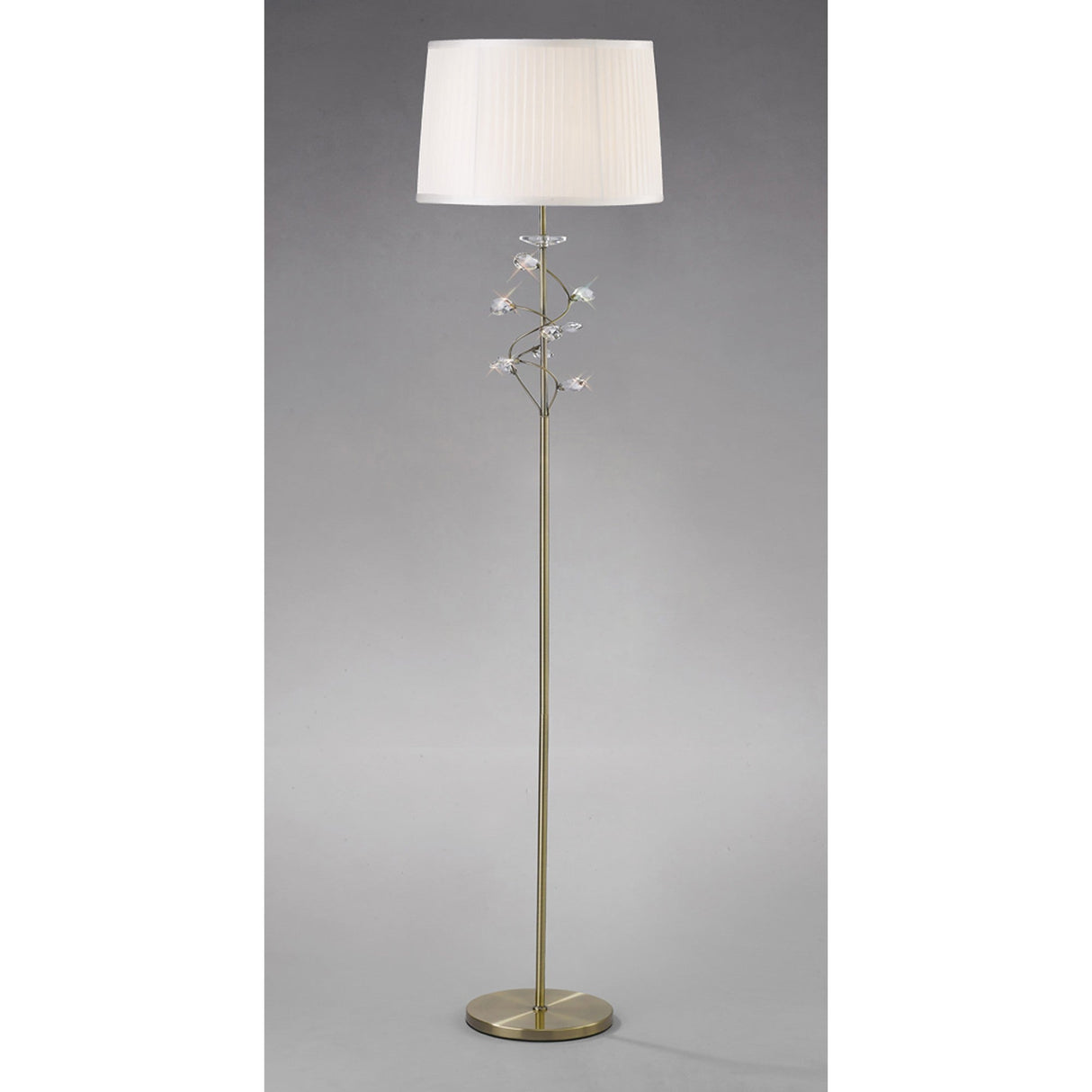 The Willow 1 Light Crystal Floor Lamp features a tall brass pole with decorative flower-shaped crystal accents, a round base, and a white fabric shade, set against a plain gray background.