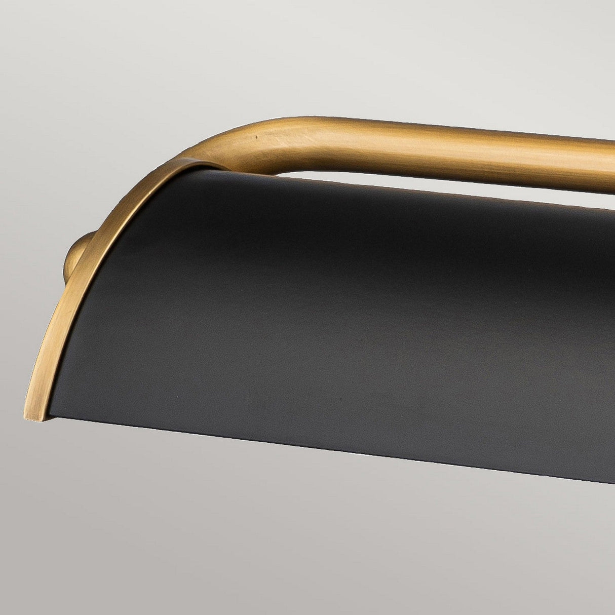 A close-up of the Winchfield 4 Light Large Picture Light showcases a sleek matte black shade with aged brass accents. Its curved design contrasts beautifully against a smooth background, embodying the essence of Mid Century Modern style.