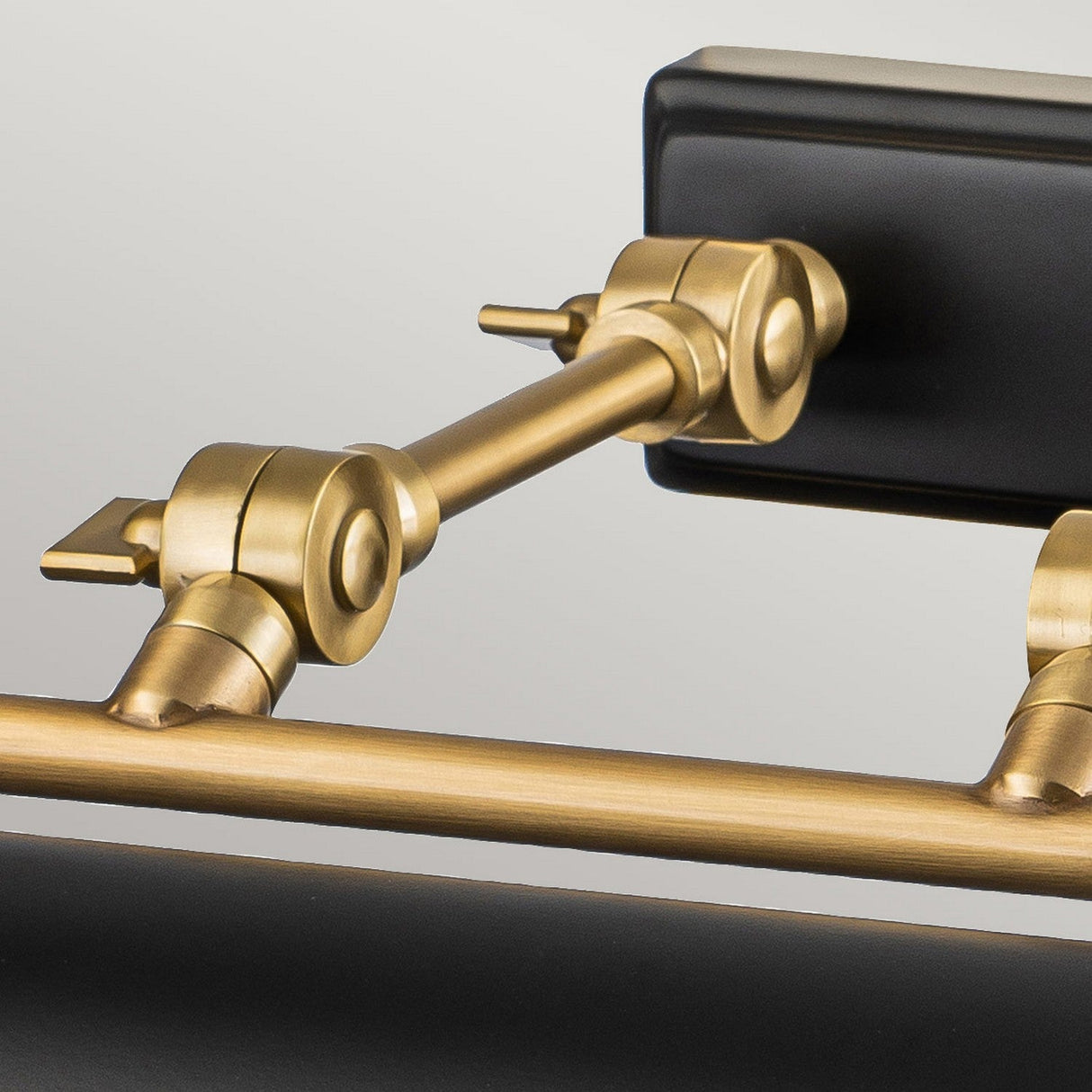 Close-up of the Winchfield 4 Light Large Picture Light in aged brass and matte black, showcasing its mid-century modern design. This adjustable fixture features joints and exudes a sleek, contemporary aesthetic against a neutral background, evoking the elegance of a classic picture light.