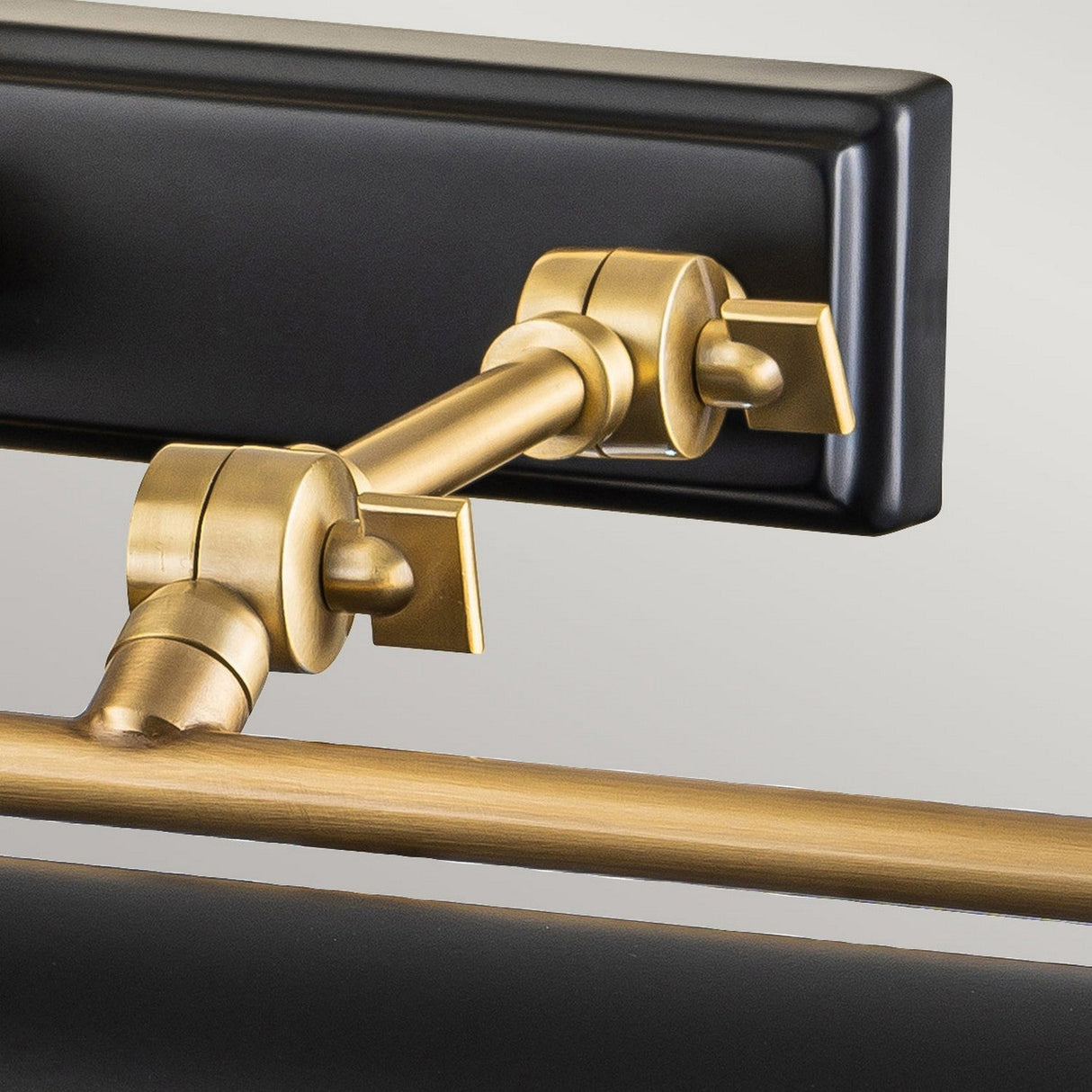 Close-up of the Winchfield 4 Light Large Picture Light in elegant aged brass and matte black, featuring an adjustable joint arm in Mid Century Modern style with geometric shapes and a modern design. The arm is attached to a rectangular black base, showcasing a combination of metallic and matte finishes.