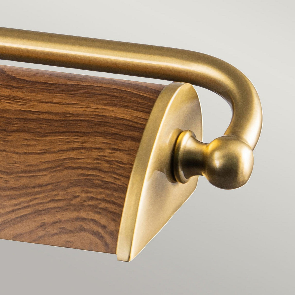 Close-up of the Winchfield 4 Light Large Picture Light in aged brass and oak effect, featuring a classic design. The fixture showcases a curved brass arm that accentuates the natural wood grain of the oak effect, all set against a light gray background.