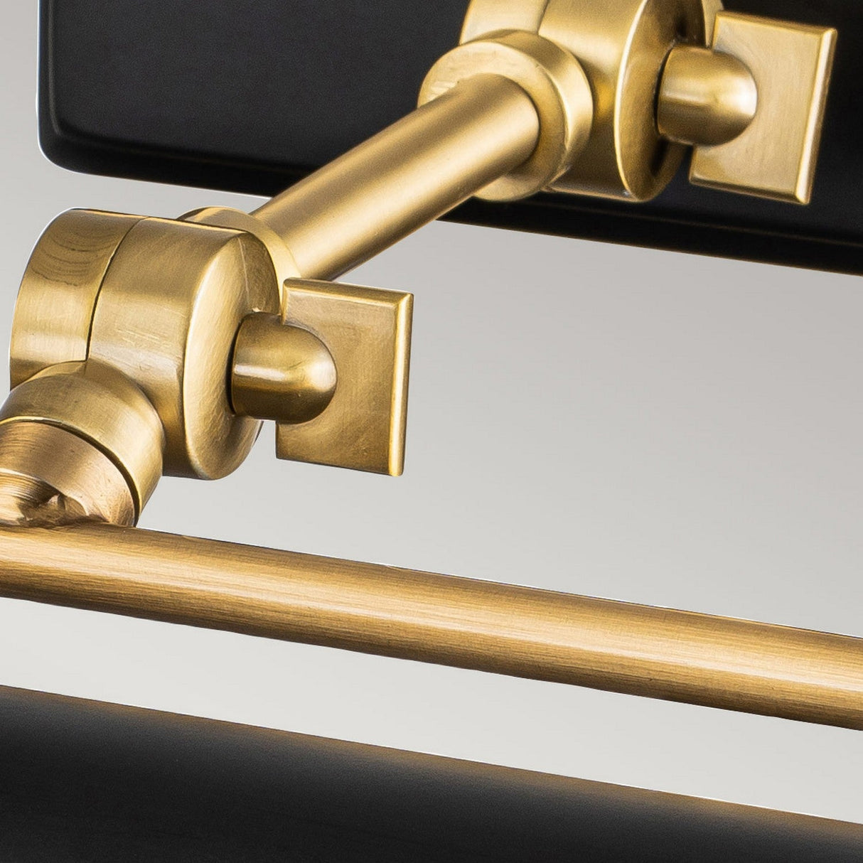 A close-up of the Winchfield 2 Light Medium Picture Light in aged brass and matte black showcases its modern wall-mounted design with adjustable joints and a sleek, rectangular silhouette. The image emphasizes the lamp's polished metal finish and elegant construction against a neutral background, making it an ideal sophisticated picture light for your space.