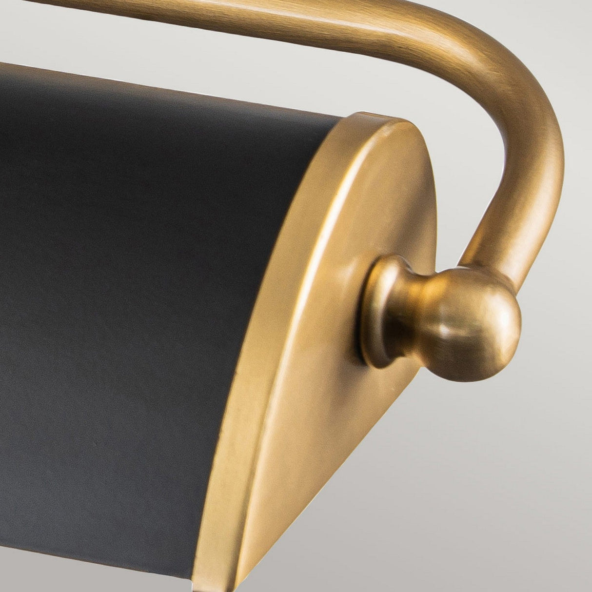 Close-up of the Winchfield 2 Light Medium Picture Light, showcasing its aged brass and matte black finish. The design features a curved, smooth gold arm and a cylindrical matte black shade, creating a sleek and elegant appearance.