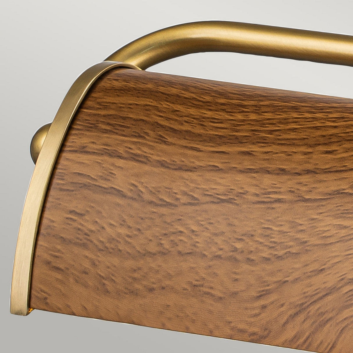 Close-up of the Winchfield 2 Light Medium Picture Light in aged brass and an oak effect finish, highlighting a carved wooden surface with a luxurious, curved aged brass handle. The smooth, rich grain of the wood contrasts elegantly with the polished finish, embodying mid-century modern style.