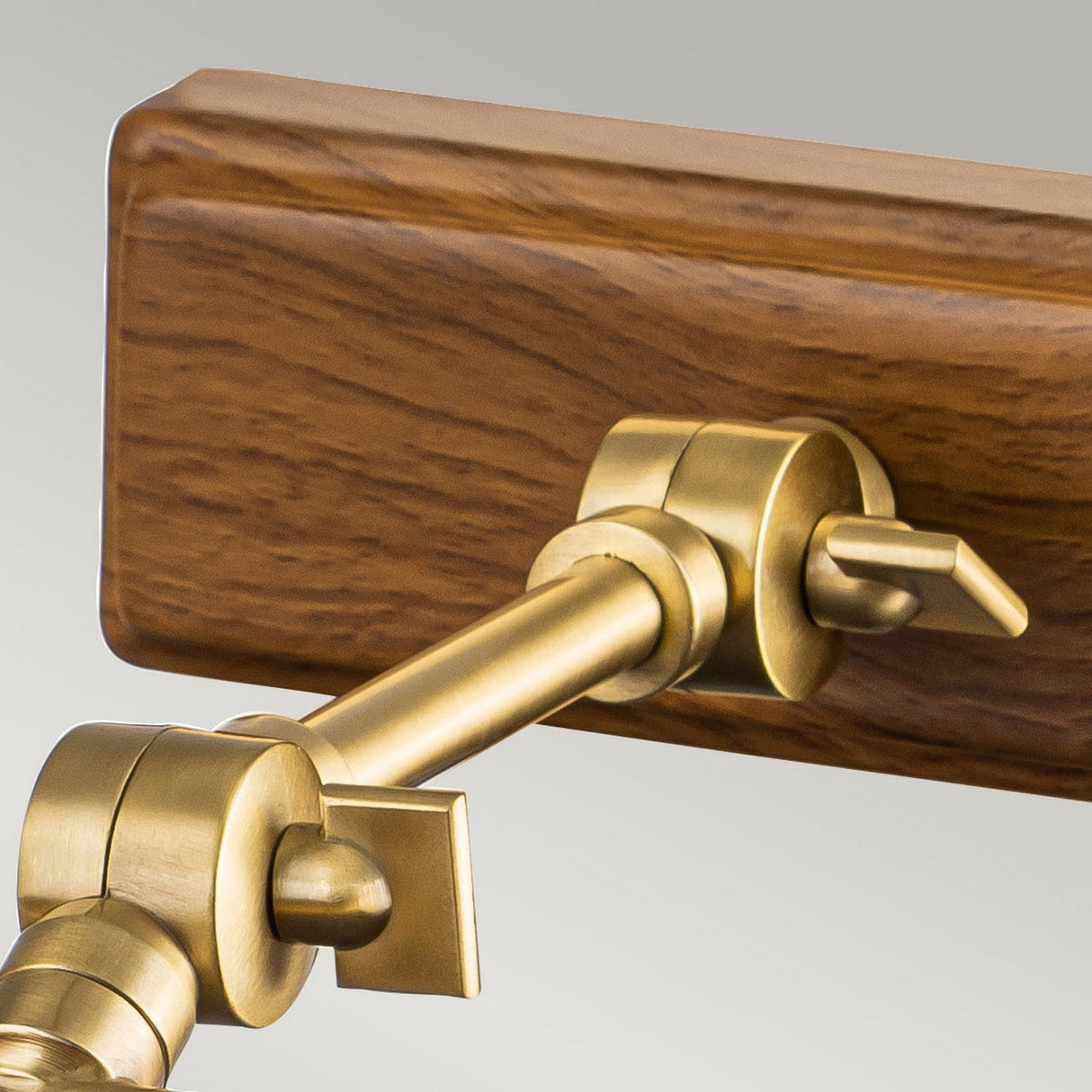 Close-up of the Winchfield 2 Light Medium Picture Light in aged brass and oak effect, featuring a wall-mounted design. It has an adjustable arm for flexible positioning, combining mid-century modern and classic elements that harmoniously blend metallic and wooden materials.