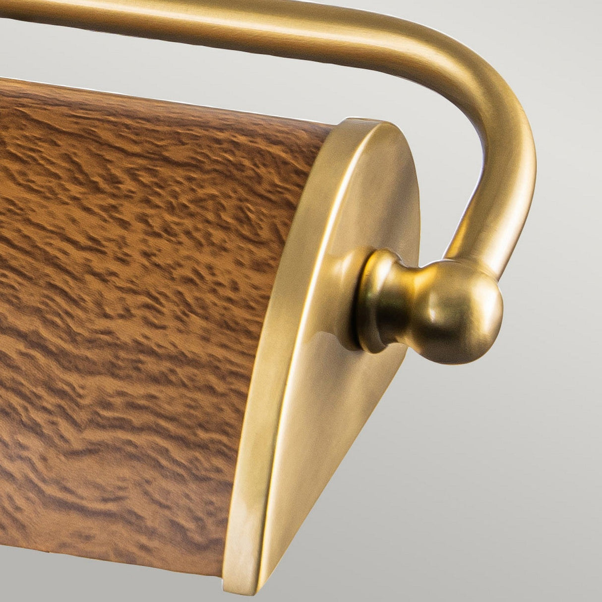 A close-up of the Winchfield 2 Light Medium Picture Light highlights its oak-effect wooden cylinder with a rich, textured grain, perfectly complemented by the aged brass handle. The smooth, rounded end of the brass evokes a sleek Mid Century Modern design set against a soft gray backdrop.