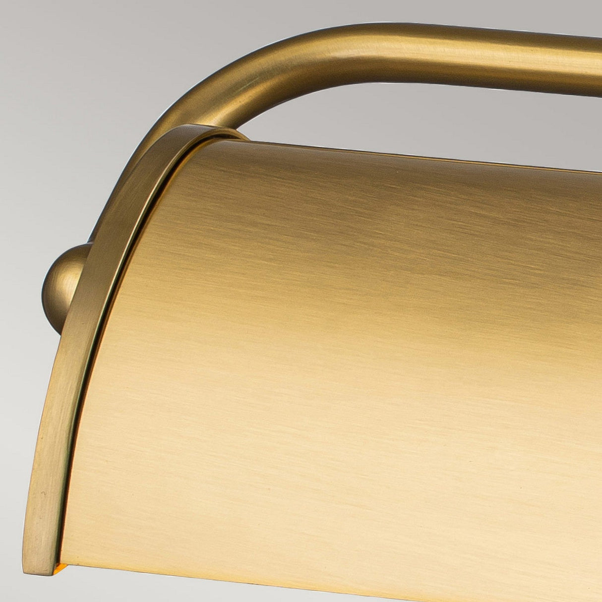 A detailed view of the Winchfield 2 Light Medium Picture Light in aged brass, showcasing its elegant metallic gold finish with a graceful curved design. The sleek surface and brushed texture give it a contemporary flair, perfectly complemented by the neutral gray background that highlights its sophisticated mid-century modern charm.