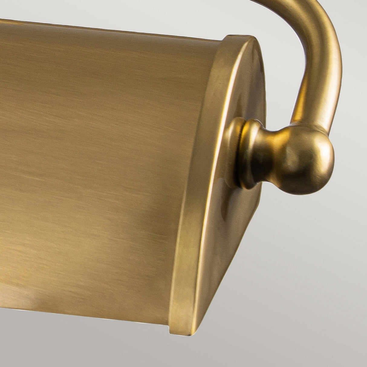 Close-up of the Winchfield 2 Light Medium Picture Light with its curved handle set against a neutral background. This mid-century modern fixture, crafted in aged brass, features a cylindrical design and brushed metal finish that enhances its elegant and vintage charm.