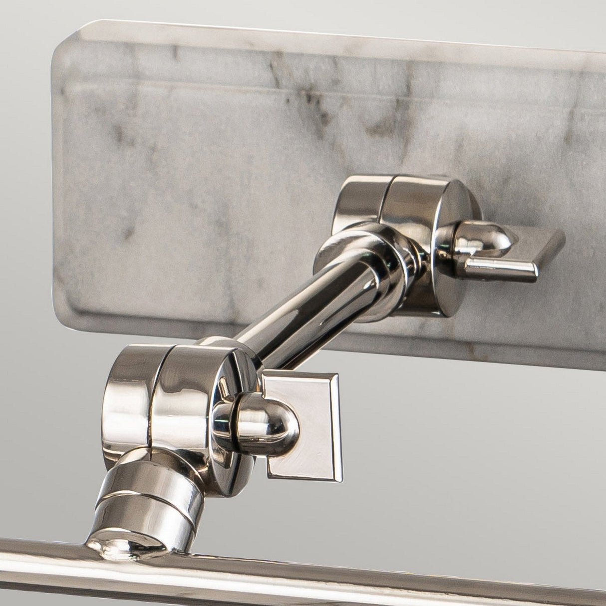 Close-up of the Winchfield 2 Light Medium Picture Light in polished nickel, exhibiting a sleek, modern design. It is mounted to a rectangular backplate with a white marble effect showcasing light gray and white patterns.