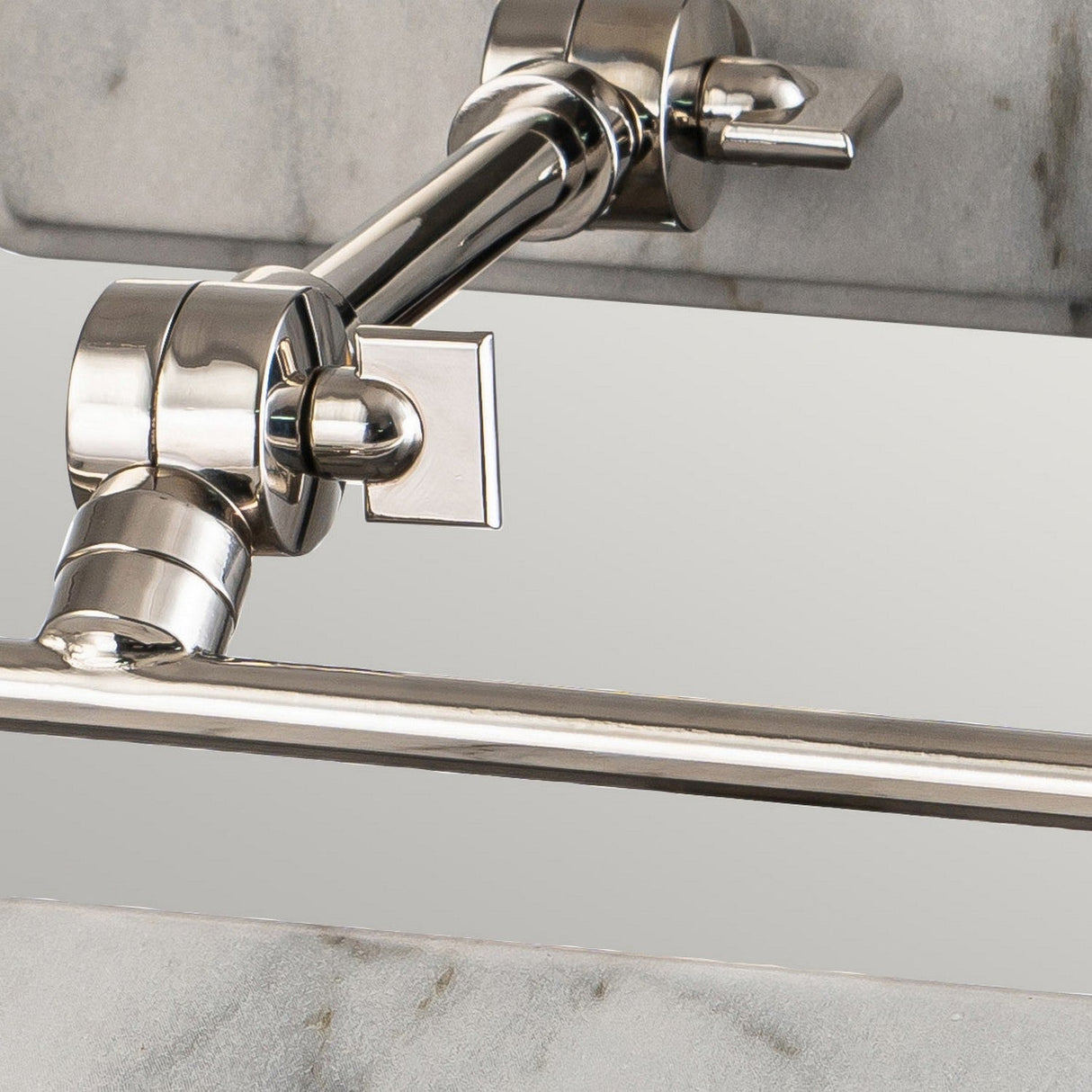 This close-up highlights the Winchfield 2 Light Medium Picture Light in polished nickel, elegantly illuminating a modern faucet mounted on a white marble effect wall. The faucet's geometric handles and sleek spout beautifully reflect the picture light, casting an artistic glow against the smooth marble backdrop.