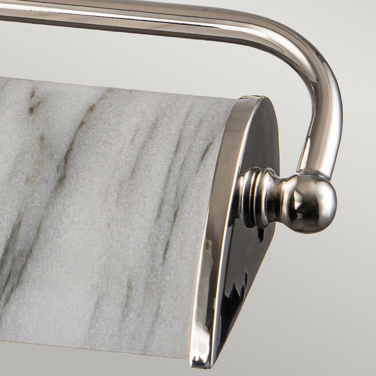 Close-up of a chrome toilet paper holder with a roll featuring a white marble effect and beige tones. The holder showcases a sleek, curved design with the polished shine similar to the Winchfield 2 Light Medium Picture Light in polished nickel, enhancing its elegant finish.