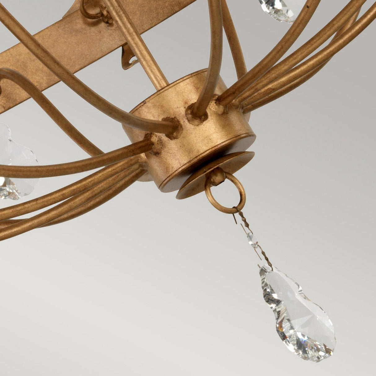 Close-up of the exquisite Windsor 12 Light Chandelier - Gold Patina, showcasing its clear crystal pendants elegantly suspended from curved metal arms. The plain light gray background accentuates the chandelier's British craftsmanship.