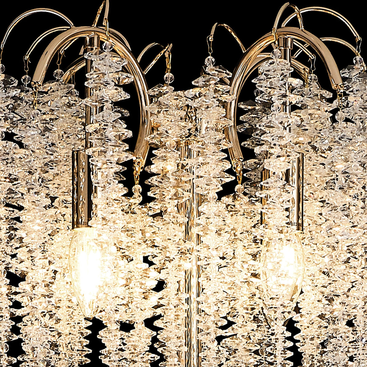 Close-up of the Wisteria 4 Light Crystal Floor Lamp in French Gold, featuring clusters of clear crystals and two glowing bulbs on a reflective metal frame, elegantly set against a black background.