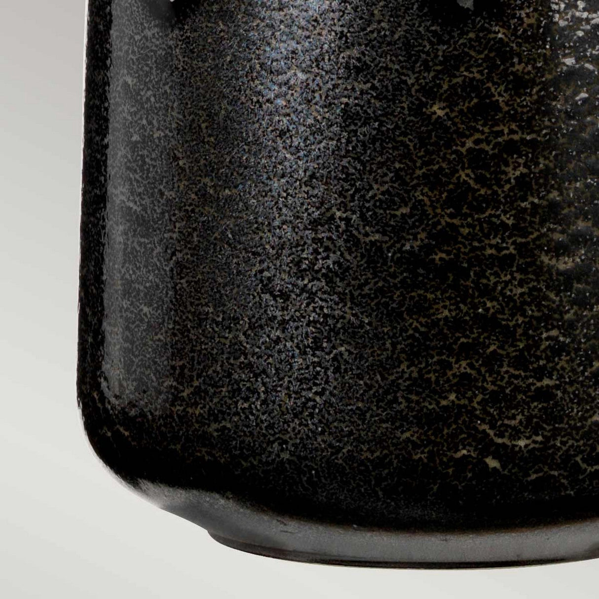 Close-up of a textured cylindrical object in graphite with a speckled surface, suggestive of the Woolwich 1 Light Table Lamp's ceramic base, against a light gray background. The object features a slightly rounded bottom edge reminiscent of table lamp designs.