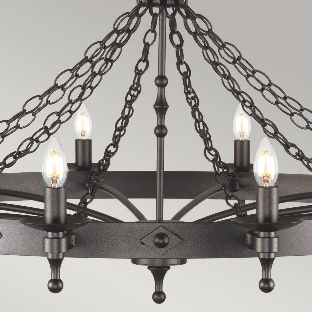 The Warwick 12 Light Chandelier - Graphite Black showcases a graphite black finish with twelve candle-like bulbs, suspended from decorative chains. Its circular and geometric design reflects medieval craftsmanship, offering a classic elegance against the light gray background.